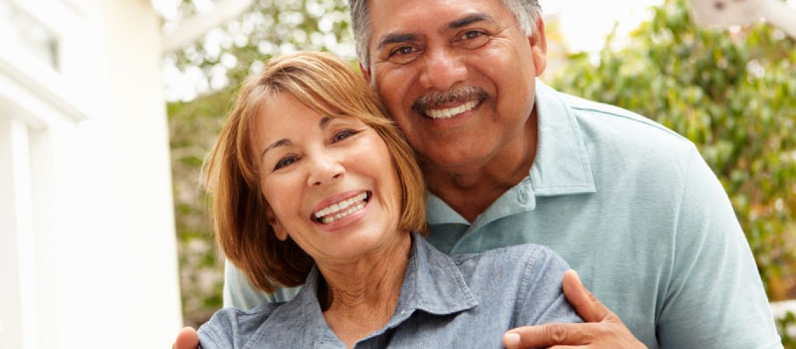two implant supported denture patients hugging and smiling.