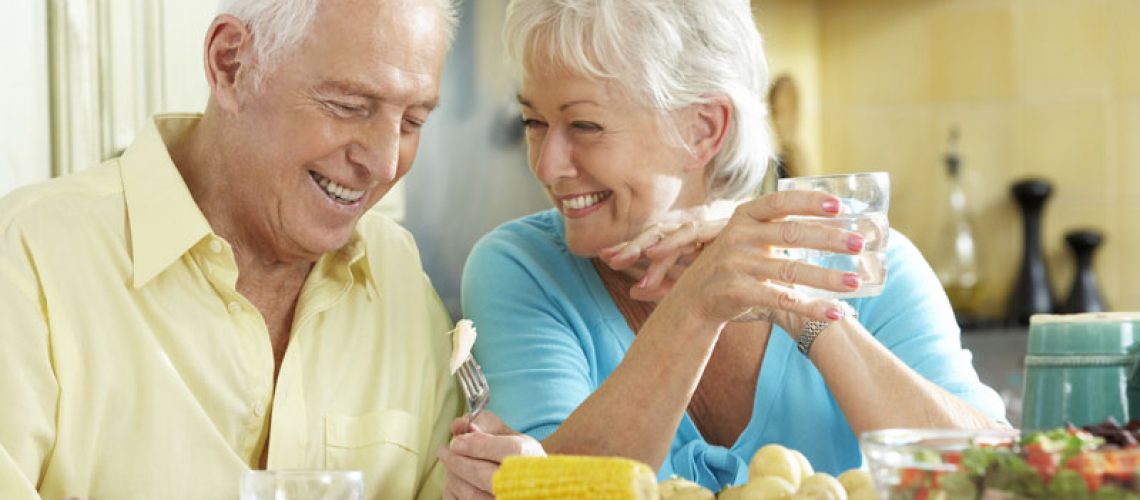 two people smiling happily at each other while they are at dinner because they have upgraded their smiles from traditional dentures to implant supported dentures.